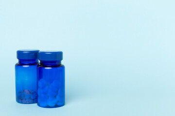 Bottles with pills and green leaves on color background