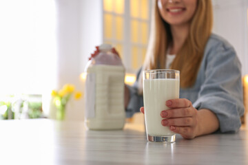 Young woman with gallon bottle of milk and glass at white marble table in kitchen, closeup. Space for text