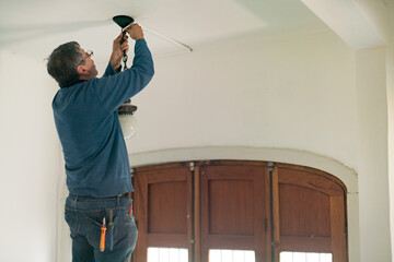 A professional energy-efficient technician on a ladder installing LED lighting on the roof of a house.