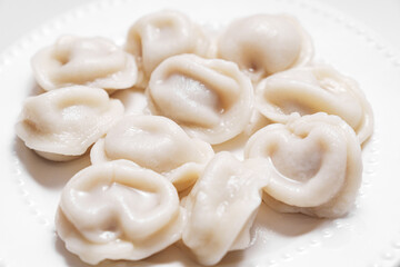 Boiled dumplings are arranged in a circle on a white plate. The plate with dumplings is set against a light background, creating a simple and appetizing composition.