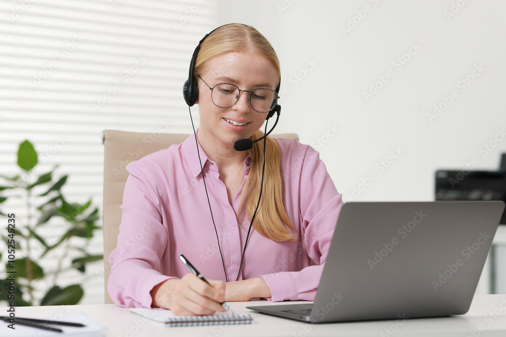 Poster interpreter in headset taking notes while working with laptop at table indoors