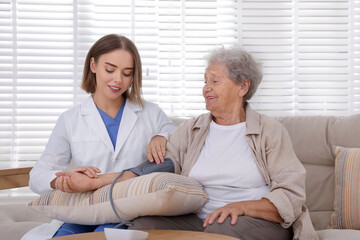 Doctor measuring patient's blood pressure on sofa indoors