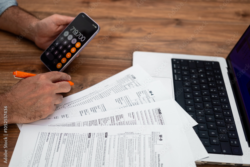 Poster man calculating taxes using smartphone and reviewing documents on wooden desk with laptop. tax prepa