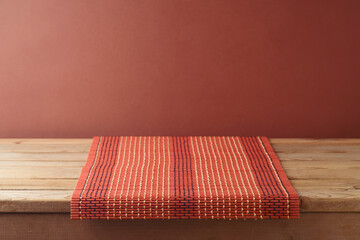 Empty wooden table with bamboo tablecloth over brown wall background. Kitchen mock up for design and product display