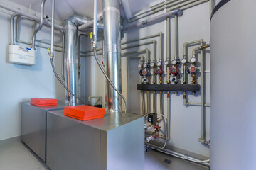A modern boiler room of a country house with a white water tank and a heating system with pipes and...