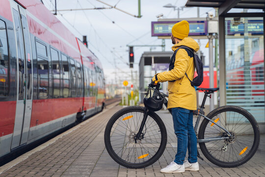 A man in winter clothes waiting with his bike for the train to arrive