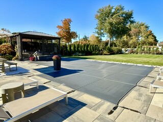 Winterized J-shaped built-in, inground pool with safety Loop - Loc mesh cover to protect it.  Allows melting snow and rain to drain through it. Brass anchors are flush to the paver height.  