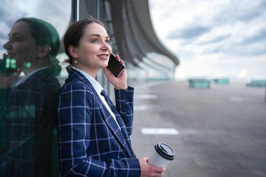 Business woman in blue checkered coat standing against glass window talking on cellphone outside