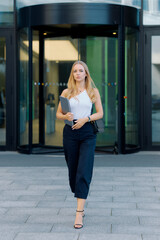Fototapeta premium Career concept, young blonde woman in white t-shirt with laptop in hands leaving office