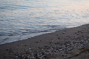 Gentle Sea Waves Touching Sandy Beach with Seashells at Sunset