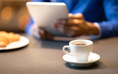 Coffee Break. Unrecognizable afro guy using tablet computer at cafe and drinking coffee, focus on cup, copyspace