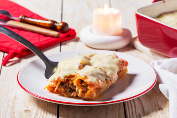 Cannellone with meat filling, tomato sauce and cheese on a light wooden table.