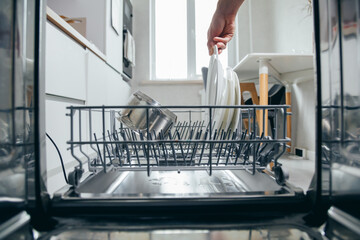 Male hand putting dirty plate in dishwasher, view from inside dishwasher. Household chores, man...