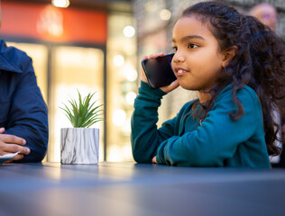 Young girl talking on smartphone at shopping mall food court table