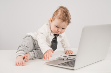 A cute child wearing a suit holds glasses and lies behind a laptop.
