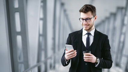 Reading News. Portrait of smiling bearded guy in suit and glasses holding cell phone and takeaway...