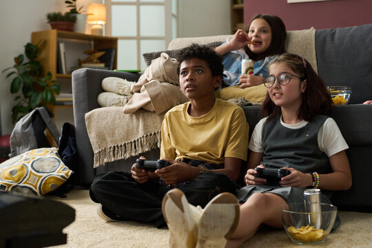 Group of friends enjoying video game session in cozy living room with snacks around. Engaged expressions while using controllers, sitting on soft couch, and having fun