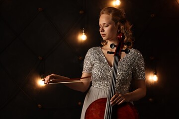 Fototapeta premium Beautiful young woman with cello on stage. Classic musical instrument