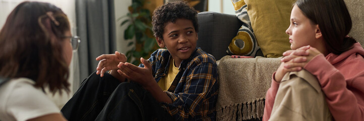 Three young friends engaged in a lively conversation while sitting in a cozy living room setting,...