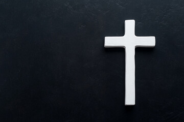 A simple white wooden cross placed on a dark textured surface. The cross is centered in the image, creating a stark contrast with the background.