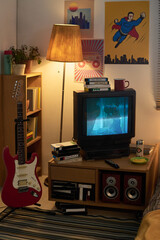 Cozy living room decorated with a mix of retro and modern art, featuring a vintage TV, guitar, wooden lamp, and bookshelf filled with books and plants
