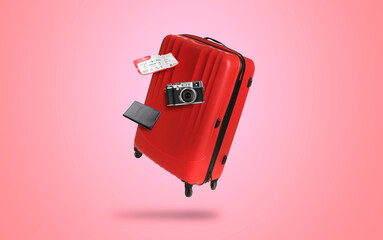 Red suitcase, camera, ticket and passport in air on pink background