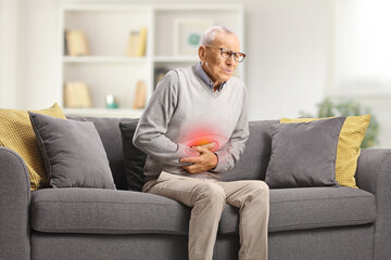 Elderly man with abdominal cramps sitting on sofa