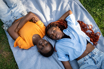 Relaxed carefree black couple of girls friends lounging, lying on blanket on grass in park. Top...