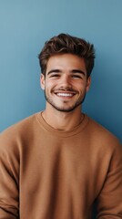 Obraz premium Cheerful young man smiling in casual sweater against a blue wall
