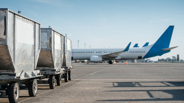 Row of aviation cargo containers on airport apron. Metal containers awaiting their turn to be loaded on passenger jet. Several airplanes visible in the background. Boryspil, Ukraine - Sept 10 2019