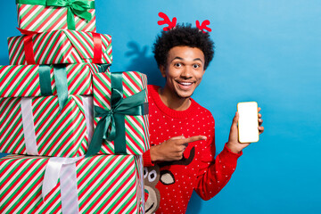 Photo of handsome guy hide pile gifts point white screen device dressed red christmas sweater...