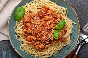 Steaming plate of spaghetti topped with a hearty bolognese sauce, garnished with fresh basil leaves, is ready to be enjoyed