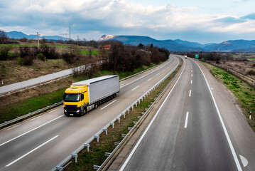 Big orange truck with a grey trailer on a countryside road in motion against an evening sky