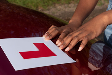 Hampshire England UK. 27.10.2024. Learner driver attaching L plate to bonnet of a red car.