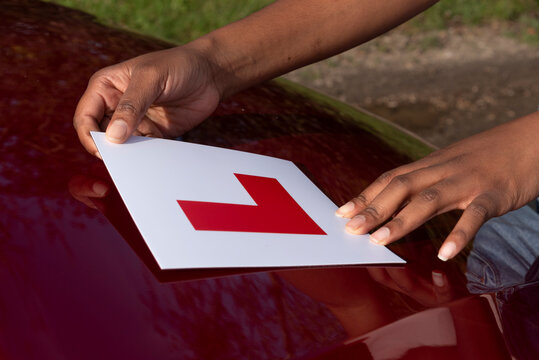 Hampshire England UK. 27.10.2024. Learner driver attaching L plate to bonnet of a red car.