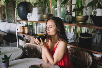 Woman in a red dress savoring the aroma of a vibrant bowl of food, eyes closed in...