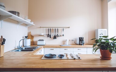 Minimalist kitchen with wooden countertop, white cabinets, and hanging utensils.