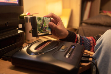 Person inserting game cartridge into retro video console in cozy living room with vintage decor and...