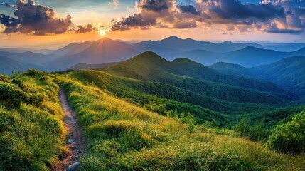 Fototapeta premium A winding path leads through a lush green mountain valley towards a distant sunset.