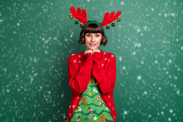 Photo of excited dreamy young lady wear print sweater horns arms chin smiling isolated green color background