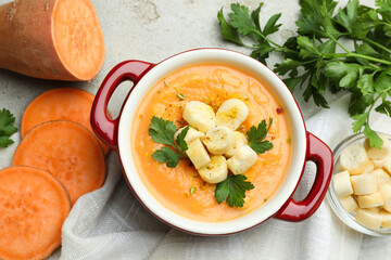 Delicious sweet potato soup with croutons and fresh ingredients on light textured table, flat lay