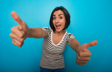 A cheerful woman with short dark hair in a striped shirt gives two thumbs up, smiling excitedly at...