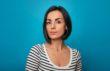 Portrait of a confident young woman with short dark hair, wearing a striped shirt, against a solid...