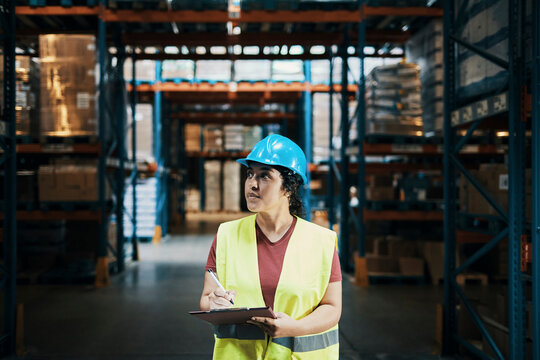 Warehouse supervisor inspecting inventory with clipboard and yellow hard hat