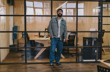 Stylish bearded male professional standing near glass wall in office