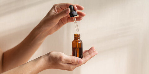 A person is holding a bottle of essential oil and a dropper. The bottle is brown and the dropper is black