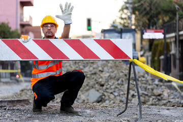 Construction worker directing traffic at roadwork site with caution barriers during the day in an...
