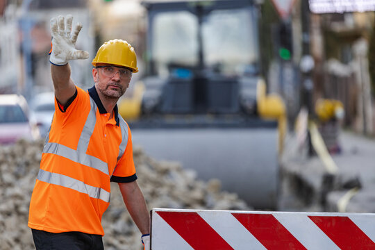 Construction worker signals for traffic to stop while directing vehicles at a roadwork site in the city during daylight hours