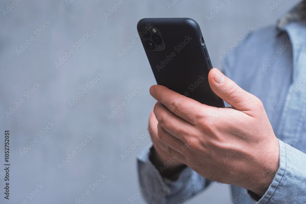 Poster man holds a mock-up of a smartphone with a dark screen close-up on a concrete background.