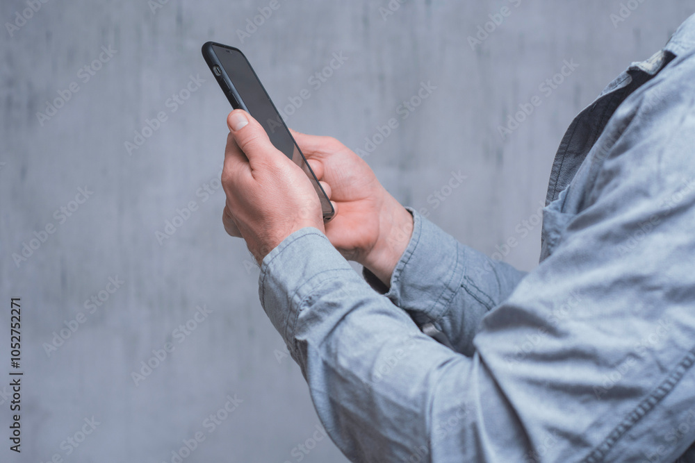 Poster man holds a mock-up of a smartphone with a dark screen close-up on a concrete background.
